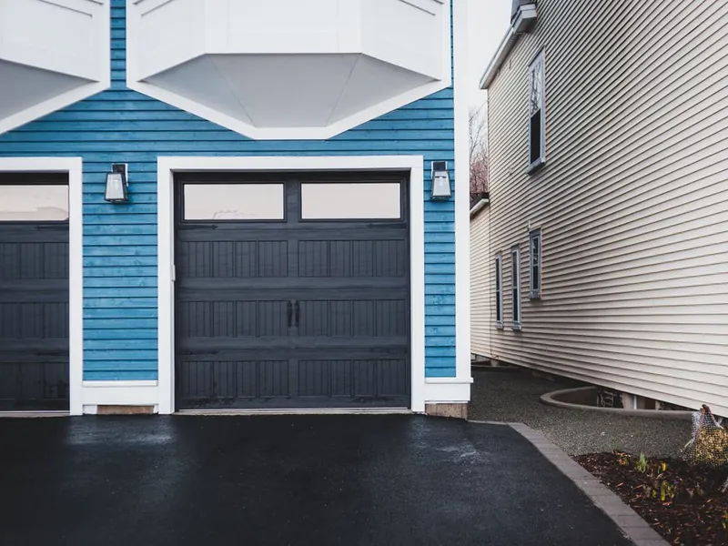 Dark carriage-style garage doors on a blue home needing spring repair